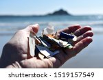 Small photo of hand holding pieces of plastic found in a few minutes beach combing on Marazion beach Cornwall UK. shows background of Mounts Bay and sea.