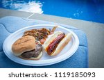 A plate of pulled pork, cheeseburger, and a hot-dog are displayed poolside. 