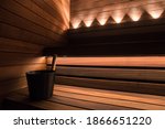 Black sauna bucket in modern design sauna with dark wood seating and LED lights.