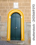 Small photo of Elvas, Portugal- October 23, 2023:Typical Portuguese facade with green door and yellow threshold. Carved stone blazon on the brick wall.