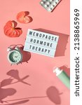 Small photo of Text Menopause Hormone Therapy, pink frame in hand. Menopause, hormone therapy concept. Estrogen replacement therapy awareness design. Pink background with exotic leaves, flowers, pills, estrogene gel