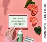 Small photo of Text Hormone Replacement Therapy, pink frame in hand. Menopause, hormone therapy concept. Estrogen replacement therapy awareness design. Pink background with exotic leaves, flowers, pills, estrogene