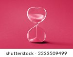 Hourglass, toned monochrome image in Viva Magenta color of the year 2023. Sandglass or sand timer. Single sand clock with golden sand on vibrant paper background. Design element,