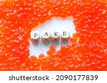 Small photo of A pile of artificial fake red caviar on a white surface next to the fake sign. Unnatural food concept. The concept of selling counterfeit products and cheating the consumer. Close-up