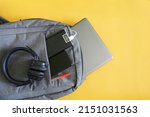Set of modern gadgets: headphones, external battery, laptop and smartphone lie in a fashionable textile backpack. Yellow background. Travel and trip concept with gadgets. Copy space. Close-up