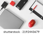 Silver laptop, computer mouse, pen, planner, portable ssd, power bank and red box on white background. Concept of a modern workplace, business planning and digital data preservation. Close-up