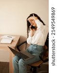 Small photo of Depressed girl overtime working online with laptop on lap and talking by phone with colleagues. Exhausted overstressed attractive young woman feeling sick and having headache