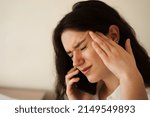 Small photo of Headache. Close-up of exhausted overstressed girl and talking on the phone. Portrait of attractive young woman feeling sick and having headache