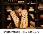 Small photo of Funny crazy cheese sommelier with 2 pieces of limited maasdam natural aged between his head. Creative worker of cheese food shop smiling, laughing and having fun