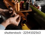 Small photo of Craftsman sews genuine leather using needle and thread for creation natural leather products. Equipment for genuine leather production in workshop. Process of stitching genuine leather
