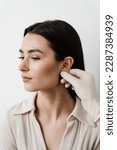 Small photo of Otoplasty ear surgery. Otoplasty surgical reshaping of pinna and ear. Surgeon doctor examines girl ears before otoplasty cosmetic surgery