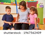 Small photo of Educator or childminder reading a book for two children in a daycare center or day nursery