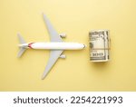Small photo of Flatlay picture of toy aeroplane, toy camera, luggage with roll fake money on yellow background. Expensive flight fare.