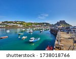 Image of Gorey Harbour with fishing and pleasure boats, the pier bullworks and Gorey Castle in the background with blue sky. Jersey, Channel Islands, UK
