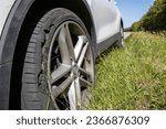 Small photo of A car with a flat tyre after a large blow out on the highway showing a large slit in the tyre at the side of the M25 motorway in London in the UK