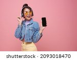 Young Asian teen woman showing smart phone she listening music in headphones isolated on pink background.	