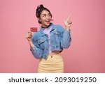 Happy beautiful Asian teen shopaholic women showing credit card and her finger pointing isolated on pink background.