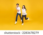 Small photo of Happy energetic Asian couple running to shopping black friday low prices summer sale isolated on yellow studio background.