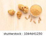 Maca root and maca powder and capsules, on white wooden background. (Taken from above)