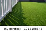 Sunlight and shadow of white wooden fence on green artificial turf surface in front yard of home, selective focus with high angle view 