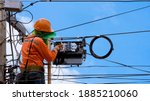 Small photo of Rear view of technician on wooden ladder checking fiber optic cables in internet splitter box on electric pole against blue sky background