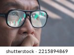 Small photo of Contemplative Asian Crypto Trader Looking at computer screen while Analyzing online Stock Trading Data Chart at home with Reflection on Eyeglasses Surface, close up with copy space