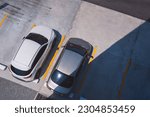 Top Angle View of 2 Cars Parked on outdoor Parking Lots area in front of building with Sunlight and Shadow on surface