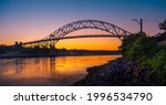 Sagamore Bridge Sunrise over Cape Cod Canal. Dawn Silhouette Architectural Image with Orange and Golden Colors. High Contrast Panoramic Seascape Image with Space for Text and Design.