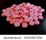 Small photo of Pink Nitroglycerin pills scattered on glossy black background - 007