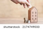 Small photo of hand of someone put coin to house money box with step of growing coins, money saving or investing for home lone or real estate concept
