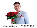Asian man wearing grey suit holding a bouquet of red roses and red gift box isolated in white background for anniversary or Valentine's day concept.
