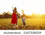 Small photo of Super mom and her son walk forward holding hands. Cheerful family, a woman in a red raincoat as a superhero. Mom and son play superheroes during the day. Friendly family concept.