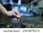 Small photo of Argentina in the hands of powerful people. Young man holds flag of Argentina near stream. Concept of humanity and dominance. Prove of depraved and avariciousness. Colour man waves with flag.