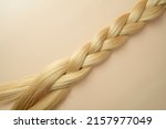 Woman's long blonde hair in the form of the tress lying on a beige background
