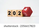 Small photo of Flipping of 2023 to 2024 on wooden block cube and white background for preparation new year change and start new business target strategy concept.