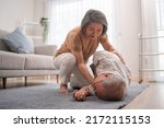 Small photo of Asian senior wife helping husband fainting and falling on the ground in the living room. Elderly male patient having an accident or heart attack. home nursing and health insurance concept