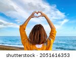 Small photo of I love you above all things! Young woman on the beach draws a heart with her hands by raising her arms to the sky. Lovely memories to be cherished.