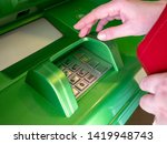 Women's hands with a red purse near the green ATM. The woman at the Bank wants to enter her pin. Women's fingers near the keyboard. Take money from an ATM.