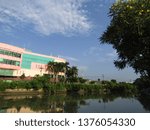 Small photo of Surabaya, Indonesia - April 21 2019: View of the back of JMP Grocery Mall Market Building with clear blue sky clouds and river background with trees around. Nearby with Red Bridge Historical Duct area