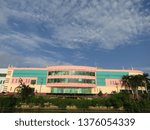 Small photo of Surabaya, Indonesia - April 21 2019: View of the back of JMP Grocery Mall Market Building with clear blue sky clouds and river background with trees around. Nearby with Red Bridge Historical Duct area