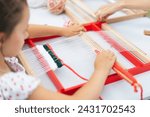 Small photo of Girl weaving small rug with pattern at masterclass on weaving. Girl is studying how to weave on manual table loom. Process of creation. Handmade concept