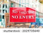 A red sign in the window of a shop displaying the message text No vaccine, no entry.