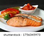 Homemade pan seared salmon steaks with grilled colorful vegetables and salsa on white plate