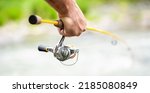Small photo of Fishings reel close-up on the background of the river. Fisherman hand holding fishing rod with reel. Fishing Reel. Fishing Rod with Aluminum Body Spool.