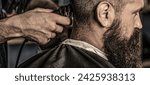 Small photo of Barber making haircut for attractive bearded man at barbershop. Hairstyle, salon, hairdresser, barber shop. Hands of barber with hair clipper. Haircut concept. Hipster client getting haircut.