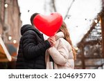 Couple holding a heart-shaped balloon and kissing on the street. Valentine's day concept, gifts, love