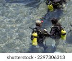 Small photo of Diving with aqualung lesson in open water. Scuba diver, instructor before diving into deep sea. Waiting on the surface before free diving. Male and women in scuba diving suit is preparing to dive