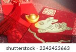 Small photo of Chinese Lunar New Year red envelope with rabbit and blessing word contained money as a gift on red background with ancient gold bullion nugget. The Chinese word means ‘happiness and good fortune’.