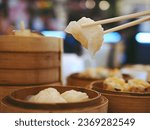 Small photo of Dim sum menu Har Gau or Har Gow, steamed shrimp dumpling in white chopsticks over blurry background of dim sum set and bokeh defocused lights. Traditional Cantonese dumpling served in dim sum.