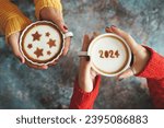 Small photo of New year 2024 celebrated coffee cup with the number 2024 on frothy surface in female hands holding over rustic blue background and another one with star symbols on frothy surface. Holidays food art.